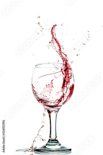 Splash of falling red wine in a round glass on a white background