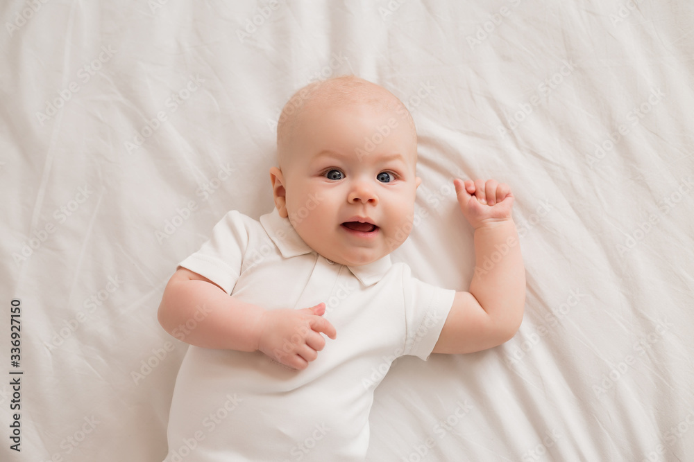Healthy toddler boy smiling in white clothes lies on the bed view from above Healthy toddler boy smiling in white clothes lies on the bed view from above