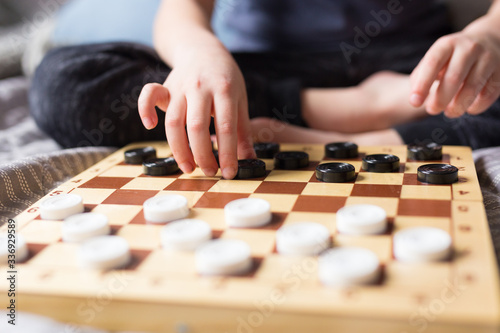 Stay at home Quarantine concept. Young kid hands playing checkers table game on bed. Board game and kids leisure concept. Family time. 