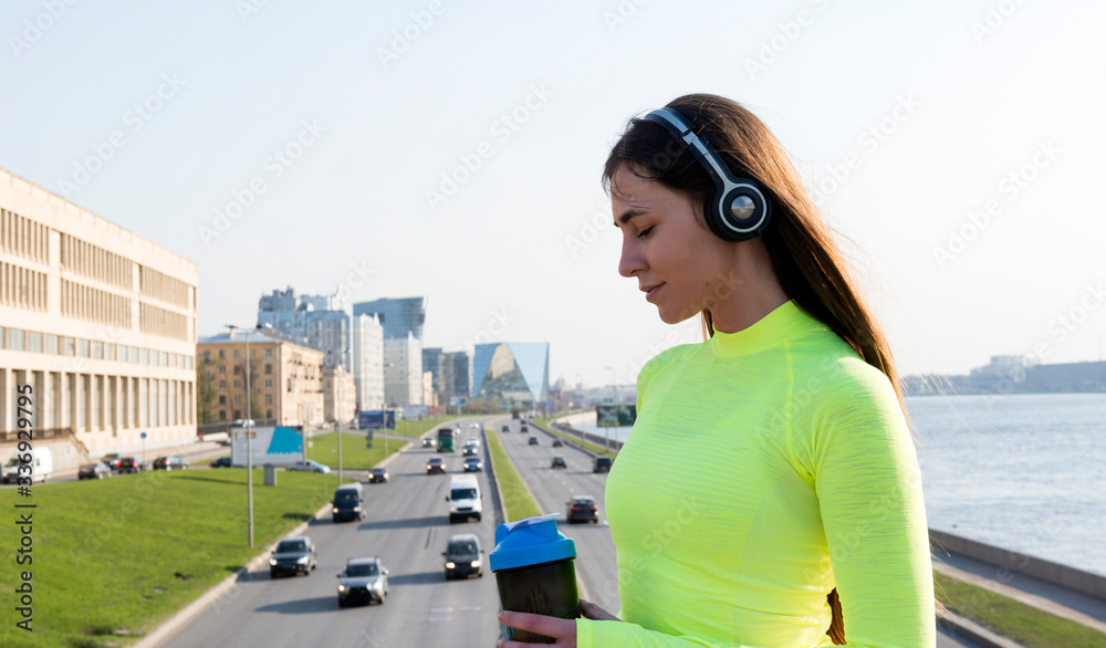 girl with long hair in a green sports top stands on a bridge over a road with cars , city and the river