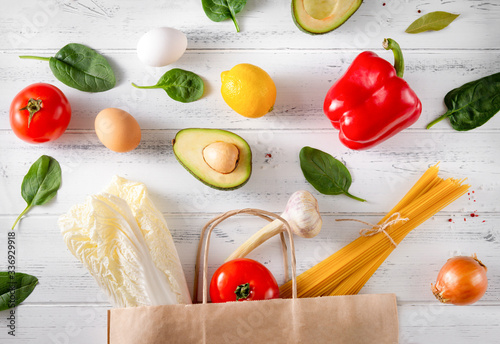 Schilderij op canvas fresh vegetables and fruit spilled from a paper grocery bag on a white wooden ba