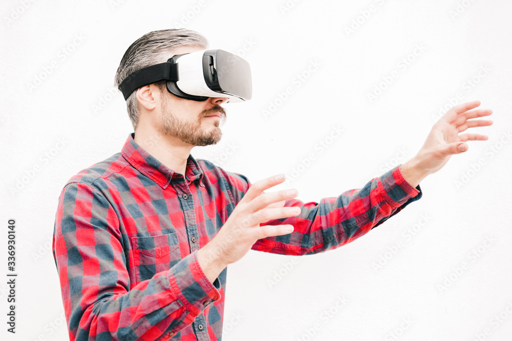 Man in VR headset touching air. Serious bearded man in checkered shirt moving with hands and using VR headset on grey background. Technology concept