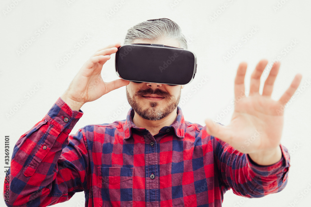 Man using virtual reality headset. Focused bearded man in checkered shirt moving with hand and using VR headset on grey background. Technology concept Man using virtual reality headset. Focused bearded man in checkered shirt moving with hand and using VR headset on grey background. Technology concept