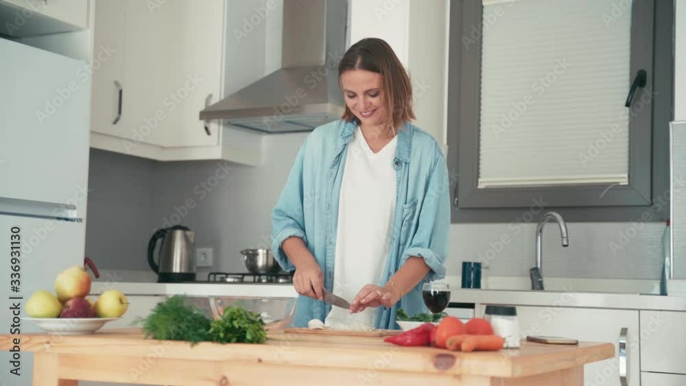 Young pretty caucasian woman cooking in her bright kitchen, cutting vegetables for the salad.