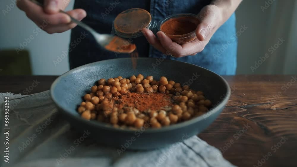 A young girl takes a spoonful of spices from a can and puts it in a bowl with chickpeas to prepare hummus. Close-up A young girl takes a spoonful of spices from a can and puts it in a bowl with chickpeas to prepare hummus. Close-up