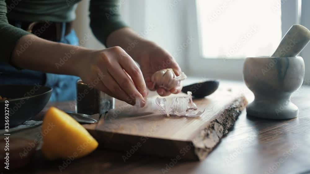 A girl peels garlic on the kitchen table to add it to the mixture of ingredients for cooking traditional hummus. Close-up A girl peels garlic on the kitchen table to add it to the mixture of ingredients for cooking traditional hummus. Close-up