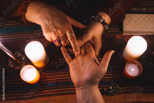 Woman reading hands with jewels on her fingers and candles and a tarot deck around the table top. Occultism concept
