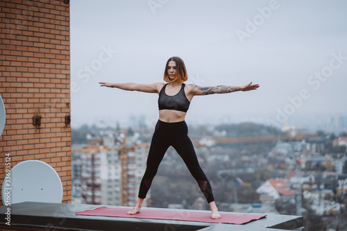 Woman practicing yoga on the mat on the roof and doing yoga exercises
