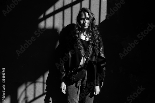 Outdoor portrait of a young woman in hard light with shadows of urban wearing trendy black jacket with incredible makeup. Black and white photography. Text space.