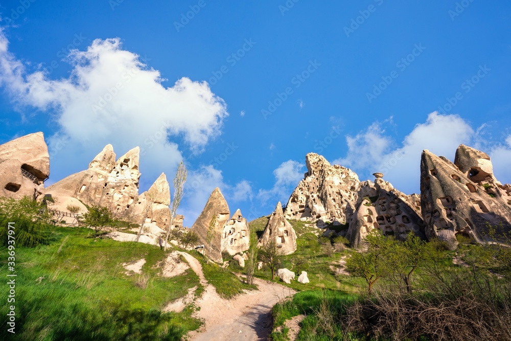 Landscape of Cappadocia, Turkey. The top of the hill is a strange sandstone mountain, inhabited by houses and has many windows. In the summer there are green grass and blue skies.