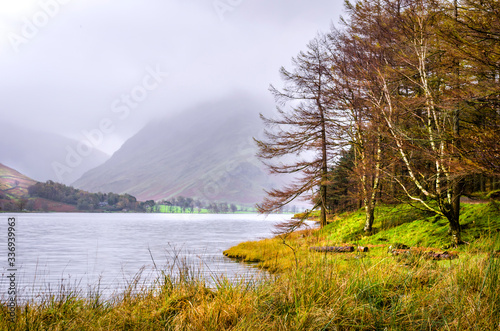 The shoreside of Lake Buttermere in the Lake District with Fleetwith Pike just visible through the mist. 