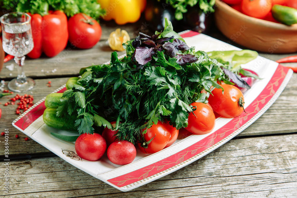Azerbaijani restaurant dish with vegetable decor on a wooden background. Sliced vegetables and herbs on a plate.