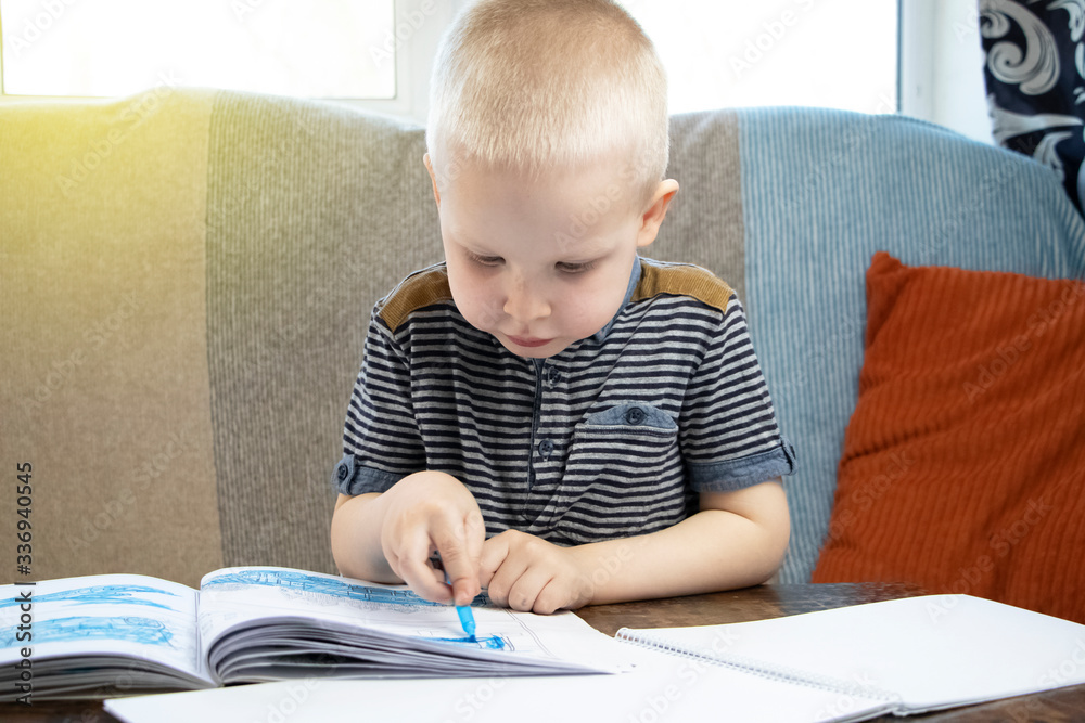 Preschooler is engaged in home schooling. The boy sits at a table, writes, draws and learns online on the Internet. Quarantine due to the coronovirus pandemic, covid-19 Preschooler is engaged in home schooling. The boy sits at a table, writes, draws and learns online on the Internet. Quarantine due to the coronovirus pandemic, covid-19