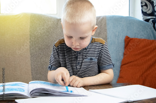 Preschooler is engaged in home schooling. The boy sits at a table, writes, draws and learns online on the Internet. Quarantine due to the coronovirus pandemic, covid-19