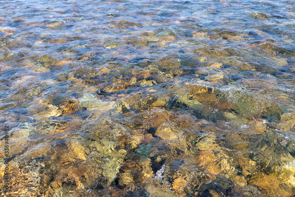 The bottom of a reservoir (river, lake) with colored stones and pebbles through clear transparent water The bottom of a reservoir (river, lake) with colored stones and pebbles through clear transparent water