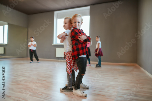 Little dancers. Two fashionable boys are standing back to back and looking at camera with smile while standing in the dance studio. Choreography class