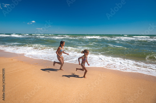Two positive little girls run along the sandy beach on a sunny warm summer day. The concept of active child rest and children's health. Copyspace