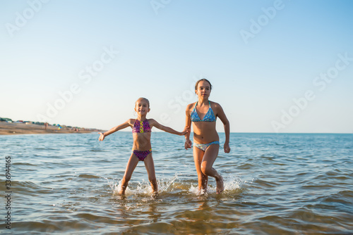 Two happy and positive girls sisters run along the sea waves during their vacation on a sunny hot summer day. Family vacation concept abroad. Copyspace © YouraPechkin