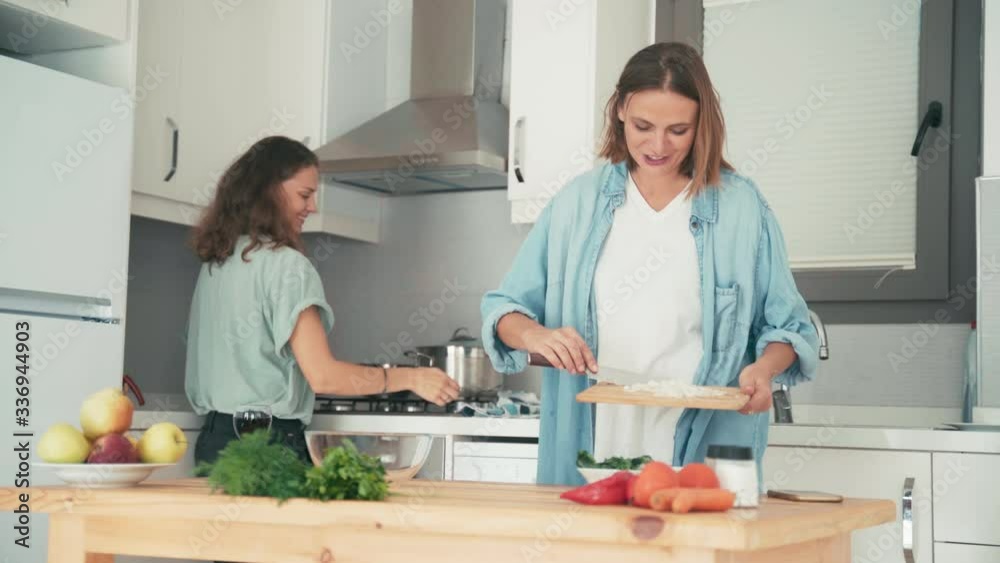 Two young pretty caucasian women cooking in the bright kitchen. Friends are having fun while cooking together. Two young pretty caucasian women cooking in the bright kitchen. Friends are having fun while cooking together.
