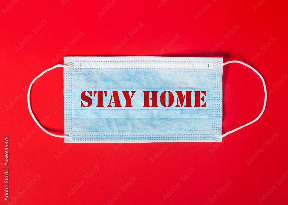 Words Stay at home on a protective medical mask on a red background. Close-up Words Stay at home on a protective medical mask on a red background. Close-up