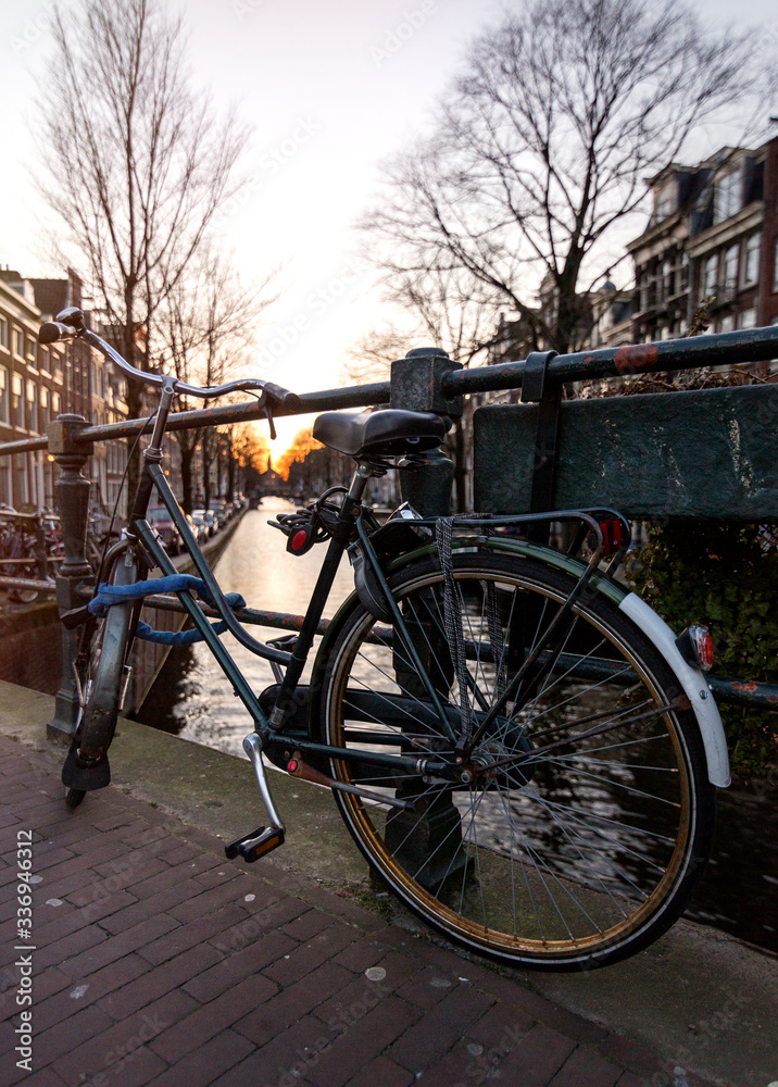 A bicycle next to a water channel in Amsterdam, with a church on the background under the sunset