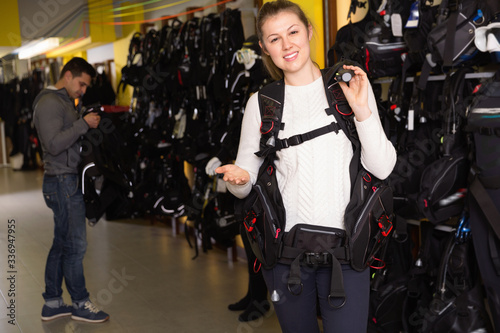 Female is standing with modern diving vest in the store.