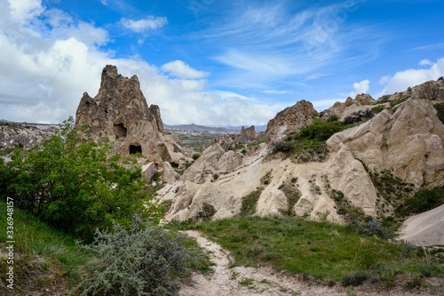 The Zelve Open Air Museum in Cappadocia, Turkey, has many sharp limestone mountains in the summer. There are green grass all over the area with blue skies.