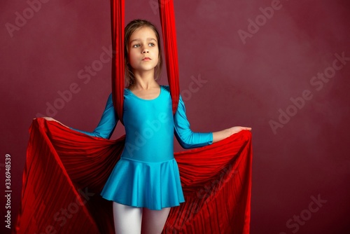 Charming little girl in a blue gymnastic suit prepared for performance with a red airy ribbon on a red-pale background. Concept sports children's acrobatics. Advertising space photo