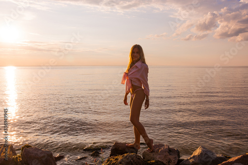 Beautiful happy young woman stands at the sea background at the sunset