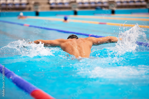 Athletic man swimming in butterfly style in the swimming pool with clear blue water.