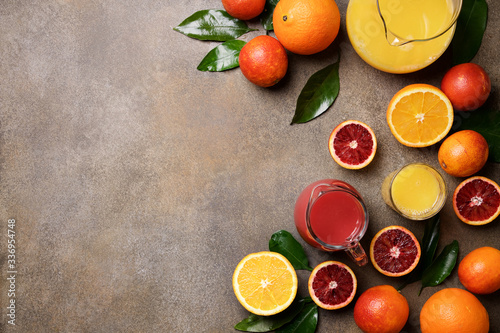 Orange juice from different oranges. Red Sicilian and orange citrus fruits. Bright background with jugs of juice and slices of fruit