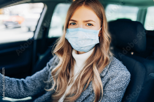 Beautiful young girl in a mask sitting in a car, protective mask against coronavirus, driver on a city street during a coronavirus outbreak