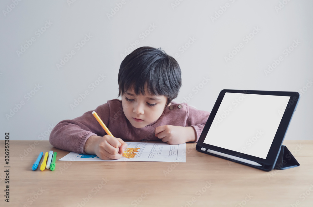 Preschool kid using tablet for his homework,Child wearing head phone doing homework by using digital tablet searching information on internet,Home schooling education concept,Social Distancing Preschool kid using tablet for his homework,Child wearing head phone doing homework by using digital tablet searching information on internet,Home schooling education concept,Social Distancing