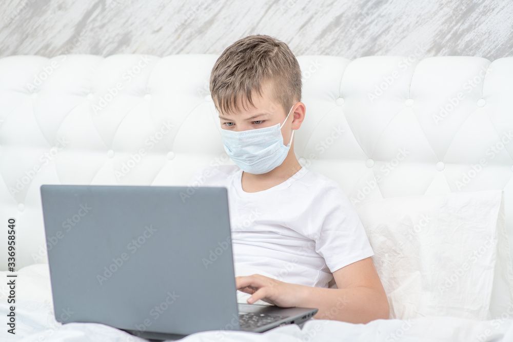 Smart boy wearing medical mask is engaged in distance learning with a laptop. Quarantine and coronavirus epidemic concept Smart boy wearing medical mask is engaged in distance learning with a laptop. Quarantine and coronavirus epidemic concept
