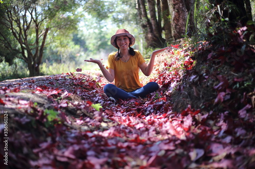 Woman sitting on the ground covered with fallen red maple leaves at Phu Kradueng National Park, Loei, Thailand