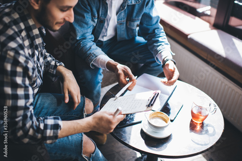 Crop freelancers discussing notes in cafe