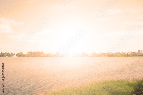 Bright white sunset over the lake and green trees. Spring