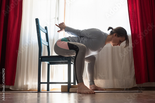 Caucasian girl workout doing Goddess Pose temple or sumo pose, stupasana, using chair sitting at home, living room. photo