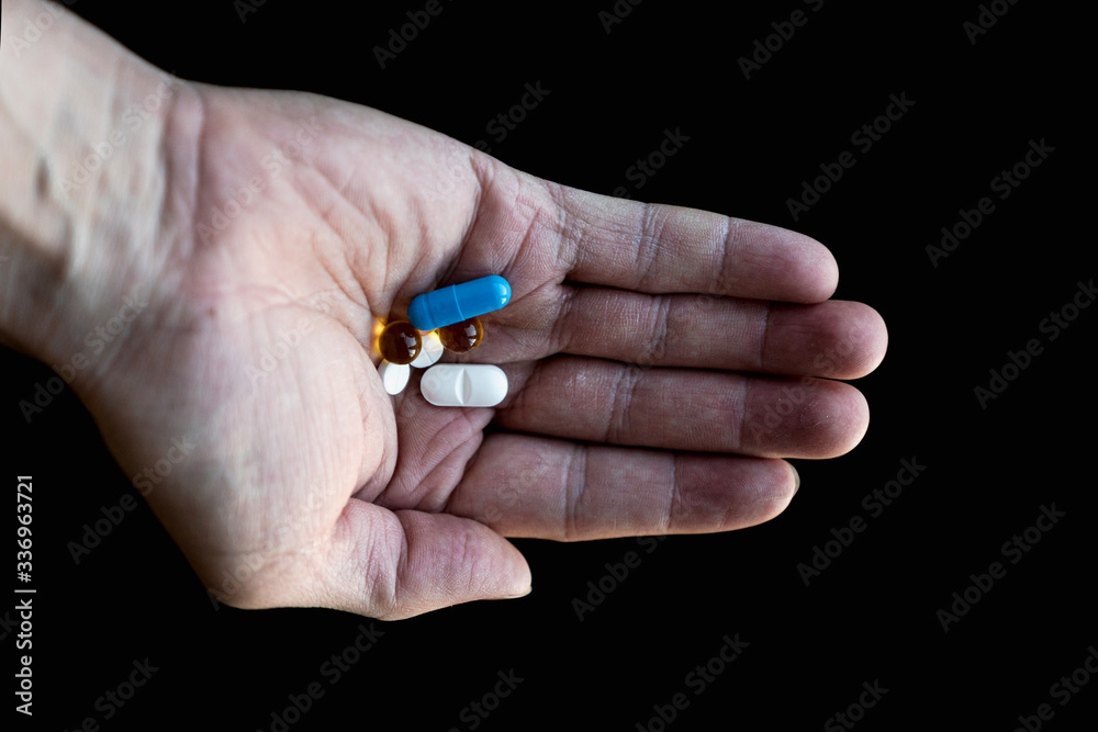 Close-up of a man's hand on a dark background, holding different tablets in the palm. Close-up of a man's hand on a dark background, holding different tablets in the palm.