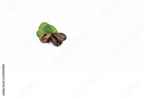 Three shiny freshly roasted coffee beans with leaves on a white background. Isolated. Selective focus.