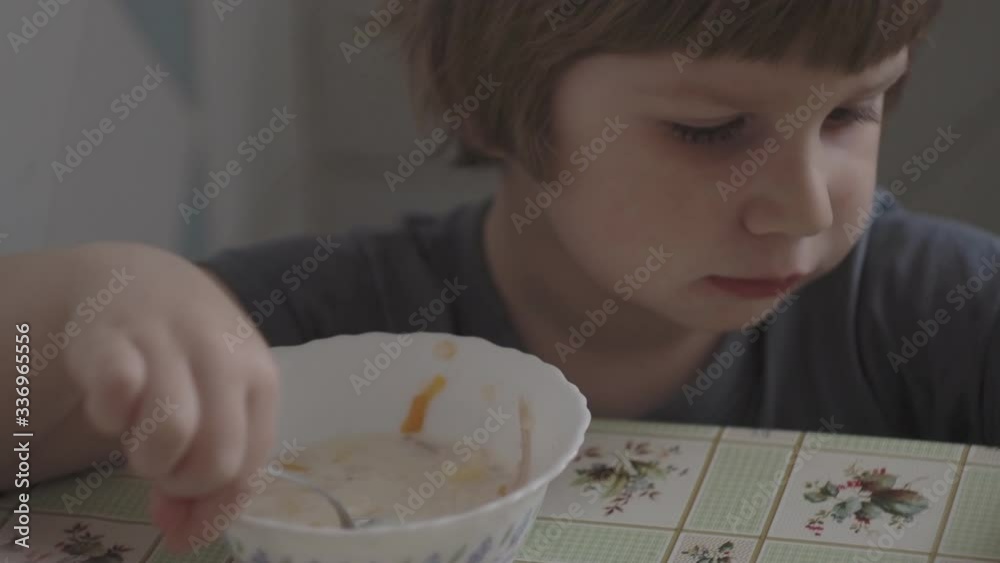 A small boy eats food at the table. A child eats food in the kitchen at the table. A small boy eats food at the table. A child eats food in the kitchen at the table.