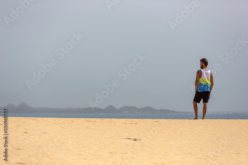 A young handsome man standing on the sand of the dunes in a beach of Fuerteventura