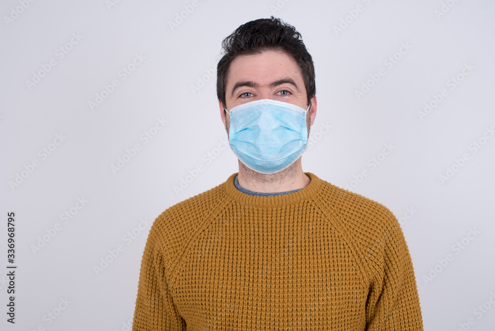 Close up studio shot of handsome young  man wearing face mask looking at camera with charming cute smile. Prevention against infectious disease.