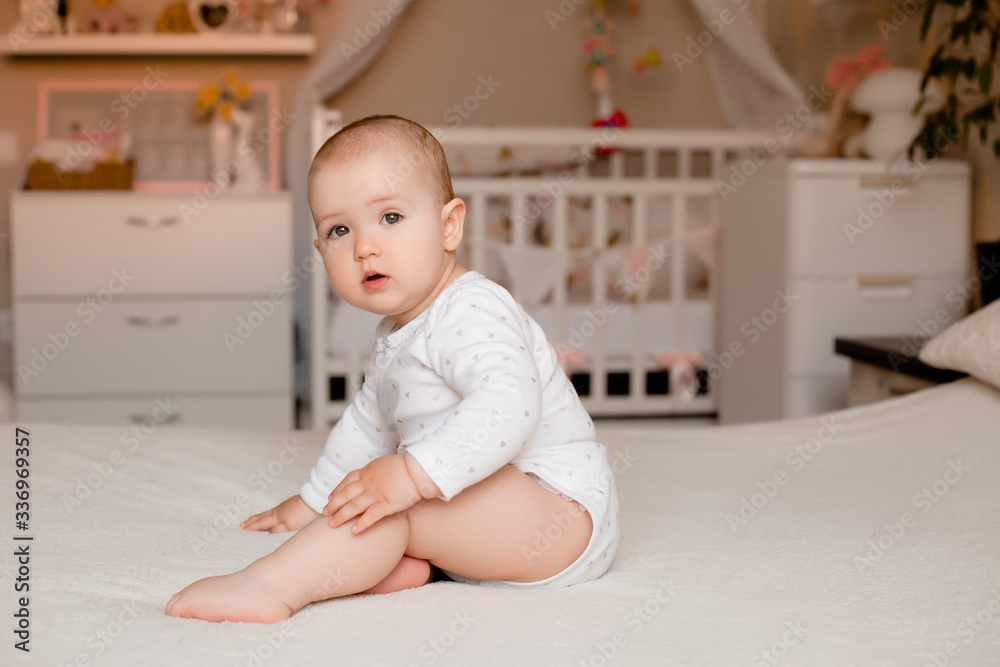 Fototapeta premium Cute little girl sits on the bed of the house in the room, space for text