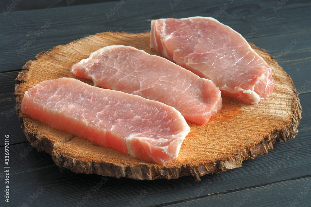 Three raw pieces of pork on a rough wooden board Three raw pieces of pork on a rough wooden board