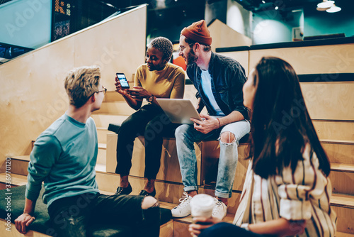 Foto Dark skinned hipster girl holding mobile phone showing app to crew of colleagues
