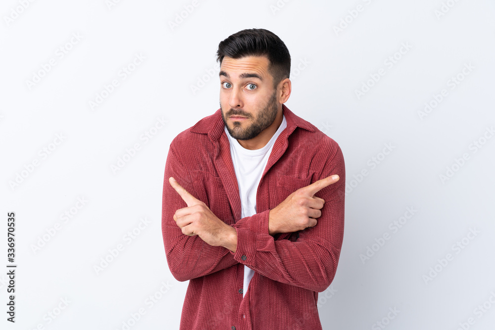 Young handsome man with beard wearing a corduroy jacket over isolated white background pointing to the laterals having doubts Young handsome man with beard wearing a corduroy jacket over isolated white background pointing to the laterals having doubts
