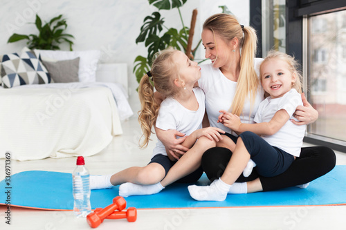 Happy mother posing at home on yoga mat with daughters