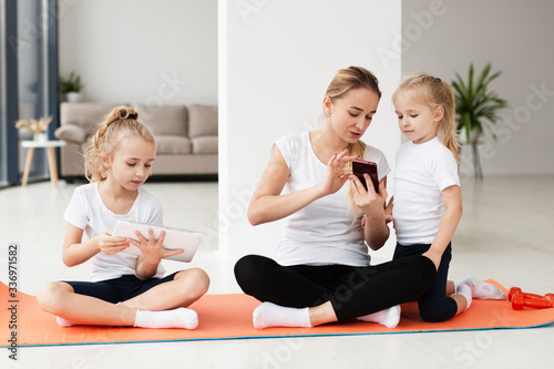 Mother showing something to daughters on smartphone while working out