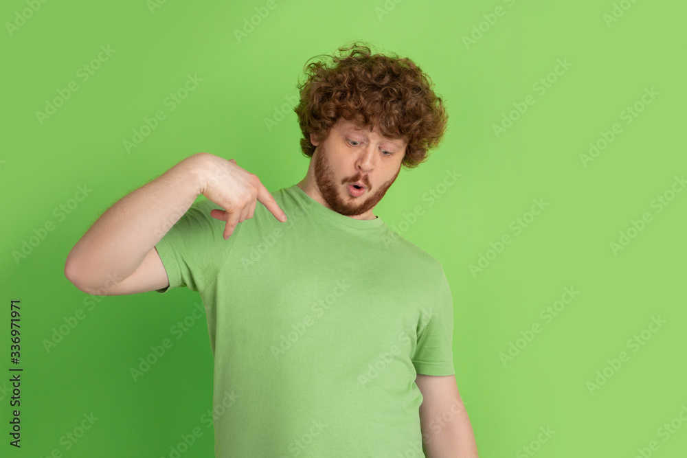 Pointing, showing, choosing. Caucasian young man's monochrome portrait on green studio background. Beautiful male curly model in casual style. Concept of human emotions, facial expression, sales, ad. Pointing, showing, choosing. Caucasian young man's monochrome portrait on green studio background. Beautiful male curly model in casual style. Concept of human emotions, facial expression, sales, ad.